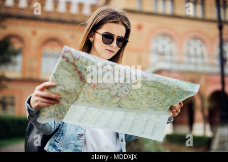 Donna allegra wanderer ricerca Direzione sulla mappa della posizione mentre si è in viaggio all'estero in estate. Felice turista femminile ricerca strada su ATLAS in una straniera Foto Stock