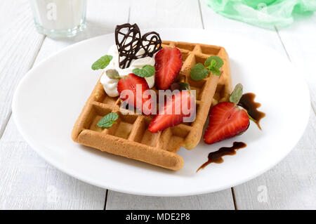 Tutto il grano cialde belghe con panna montata, tritato fresco Fragole, foglie di menta e cioccolato bianco su sfondo di legno. Le sane b Foto Stock