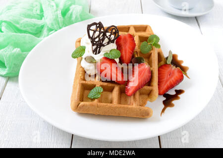 Tutto il grano cialde belghe con panna montata, tritato fresco Fragole, foglie di menta e cioccolato bianco su sfondo di legno. Le sane b Foto Stock