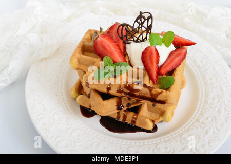 Tutto il grano cialde belghe con panna montata, tritato fresco Fragole, foglie di menta e cioccolato bianco su sfondo di legno. Le sane b Foto Stock