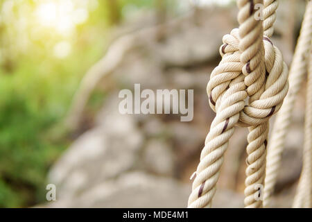 Close-up di corda linea di nodi legati insieme con il ponte sullo sfondo. Corda bianco legato con un nodo per l'avventura.corda, legare un nodo legato ad una maglia di palo metallico Foto Stock