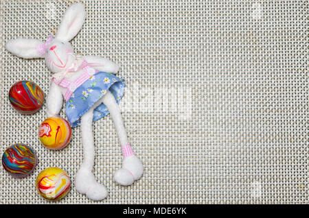Concetto di Pasqua, peluche coniglietto di Pasqua sulla paglia con sfondo decorato, uova colorate. Foto Stock