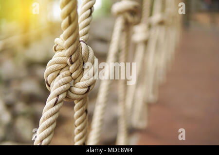 Close-up di corda linea di nodi legati insieme con il ponte sullo sfondo. Corda bianco legato con un nodo per l'avventura.corda, legare un nodo legato ad una maglia di palo metallico Foto Stock