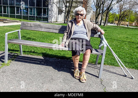 Una signora anziana seduta su una panchina del parco, una donna anziana da sola Foto Stock