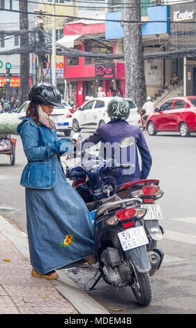 Una donna vietnamita indossando giacca denim, abbigliamento e guanti, utilizzando il proprio telefono cellulare con la sua moto, nella città di Ho Chi Minh, Vietnam. Foto Stock