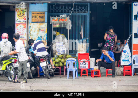 Motociclisti parcheggiare la propria moto sul marciapiede e un vietnamita uomo seduto su uno sgabello in plastica parlando sul suo telefono mobile e avente un drink. Foto Stock