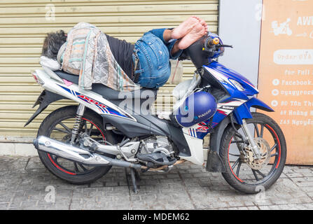 Un uomo dorme mentre equilibrata su un motociclo in Ho Chi Minh City, Vietnam. Foto Stock