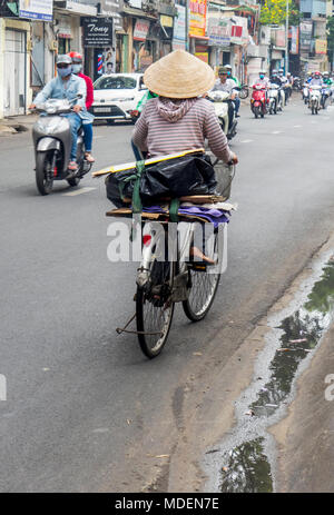 Una femmina vietnamita ciclista indossando un cappello conico in sella la sua bicicletta su una strada nella città di Ho Chi Minh, Vietnam. Foto Stock