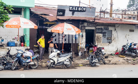 Motociclo vietnamita meccanica lavorando sul marciapiede e permanente del client al di fuori del laboratorio in Ho Chi Minh City, Vietnam. Foto Stock