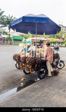 Un motore ciclista fermo sulla strada per comprare mare noci di cocco e palme Nipa per la vendita sul ciglio della strada nella città di Ho Chi Minh, Vietnam. Foto Stock