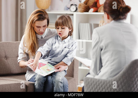 Madre con bambino autistico tenendo un disegno durante la consultazione con la psicoterapeuta Foto Stock