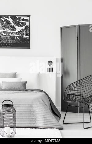 Lanterna e poltrona nera in camera da letto moderno interno con poster sopra il letto accanto a una schermata Foto Stock