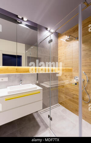 Moderno bagno interno con doccia in vetro cabina, grigio scuro piastrelle, specchio e lavabo bianco Foto Stock