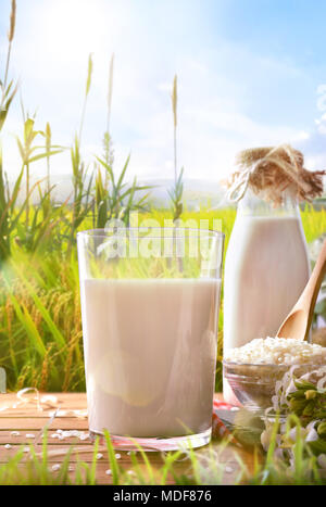 Composizione con la bevanda di riso su base di legno nel campo. Latte alternativi. Vista frontale. Composizione verticale Foto Stock