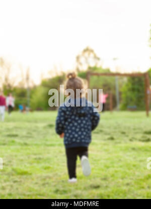 Inquadratura sfocata .bambina corre da dietro al parco a giocare con gli altri bambini. Foto Stock