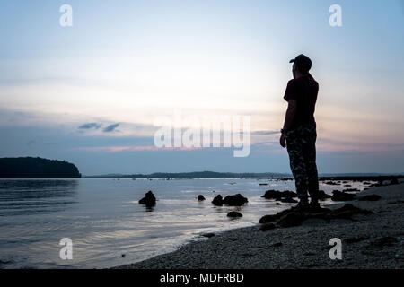 Silhouette di un solo uomo che guarda verso la vibrante del tramonto. Flare e riflessi in acque poco profonde del livello del mare Foto Stock