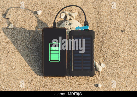 Portatile pannello solare è sulla spiaggia in sabbia e carica la batteria della cornice cellulare. uso di energia solare nel selvaggio su un deserto è Foto Stock