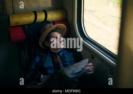 Giovane uomo ubicazione su un treno con una mappa Foto Stock