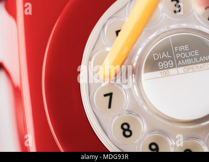 Close up di retro rosso dagli anni sessanta agli anni settanta telefono con matita gialla in bilico per comporre il numero. Foto Stock