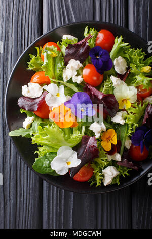 Insalata mista di fiori commestibili con lattuga, pomodori e crema di formaggio vicino sul tavolo. Verticale in alto vista da sopra Foto Stock