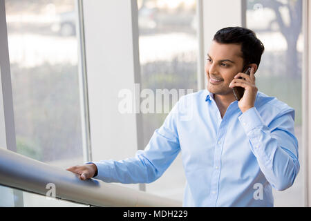 Un primo piano ritratto di una giovane occupato, felice e sorridente uomo d affari di parlare sul suo telefono cellulare mentre si cammina sulla costruzione di ufficio scalinata, isolati su indoo Foto Stock