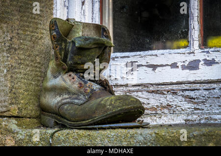 Un vecchio boot seduto su una battuta di cemento al di fuori di una finestra a spiovente; Clapham, North Yorkshire, Inghilterra Foto Stock