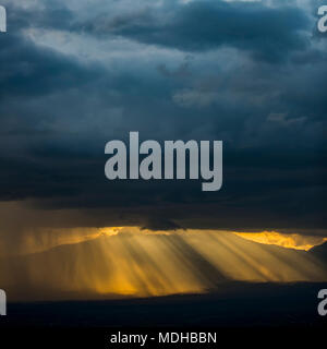 Golden raggi di sole e pioggia illuminato che brilla attraverso il buio, inquietanti nubi con montagne in lontananza, Parco Nazionale Vulcani delle Hawaii Foto Stock