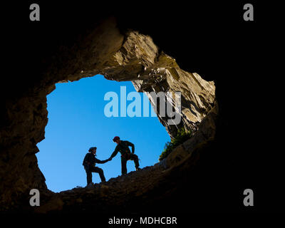 Una giovane coppia di arrampicata in bocca di una grotta, tenendo le mani per il supporto; Fernie, British Columbia, Canada Foto Stock