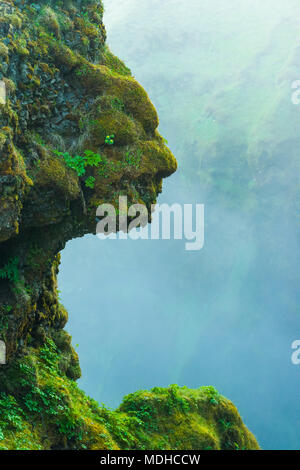 La forma della testa in rocce naturali coperte di muschio verde accanto a cascata Skogafoss; Islanda Foto Stock