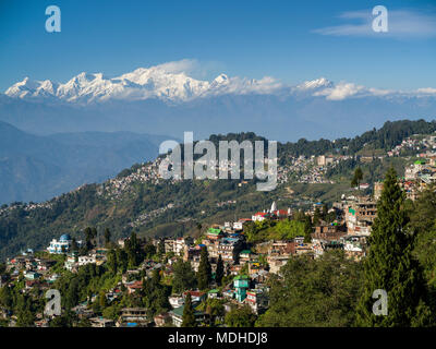 La città sul versante di una montagna con il robusto, cime innevate dell'Himalaya in distanza; Darjeeling, West Bengal, India Foto Stock