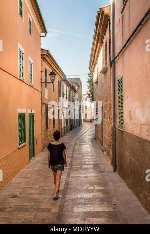 Donna che cammina giù per una strada stretta; Alcudia Maiorca, isole Baleari, Spagna Foto Stock