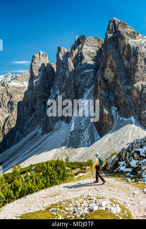 Escursionista femmina sul sentiero con la sottostante valle contro una robusta gamma di montagna e cielo blu; Sesto, Bolzano, Italia Foto Stock