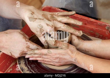 Le mani di due persone creare vaso sul tornio del vasaio. Insegnamento in ceramica, carftman con le mani in mano la guida Foto Stock