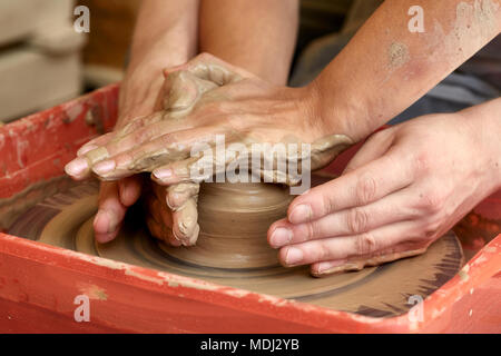 Le mani di due persone creare vaso sul tornio del vasaio. Insegnamento in ceramica, carftman con le mani in mano la guida Foto Stock