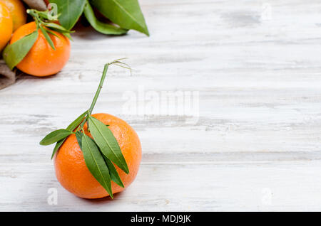 Freschi organici grezzi Mandarini Clementine con foglie verdi nel sacco bianco su un tavolo di legno., spazio di copia Foto Stock