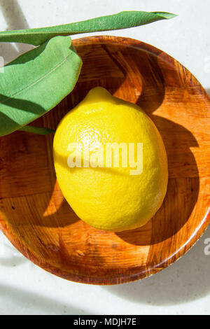 Mature limone giallo verde delle foglie nel recipiente di legno su marmo bianco dello sfondo. La luce diretta del sole. Cosmetici biologici Ayurveda e uno stile di vita sano concetto. Authe Foto Stock