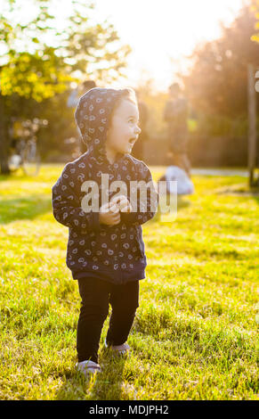 Piccola bambina gioca felice nel parco all'aperto nella primavera in controluce. Foto Stock