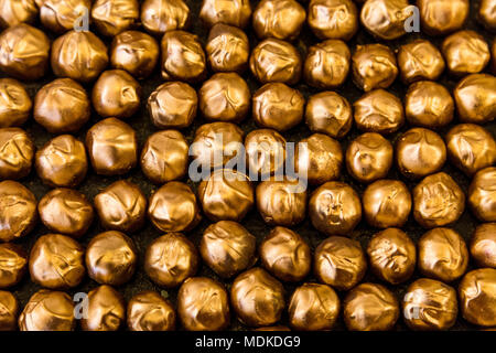 Righe di praline di cioccolato nel rivestimento dorato sfondo scuro (zuccheri cacao House, Londra, Regno Unito) Foto Stock