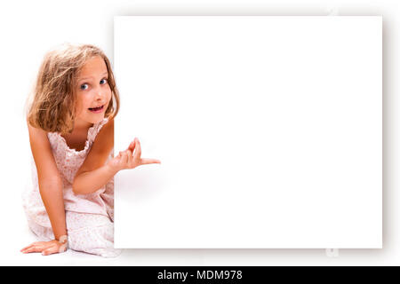 Sorridendo felice 7 anni ragazza guarda outs e puntamento dal vuoto banner. Foto Stock