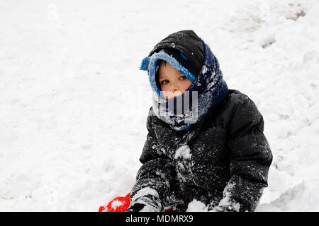 Ritratto di un giovane ragazzo (5 yr old) vestita in outdoor abbigliamento invernale e coperto di neve Foto Stock