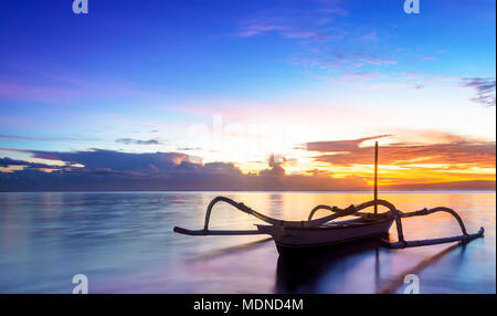 Jukung bali tradizionale barca da pesca su sunrise vicino a Sanur Beach affacciato sull'oceano. Lo stile tradizionale canoa è equipaggiato con due bambù Foto Stock