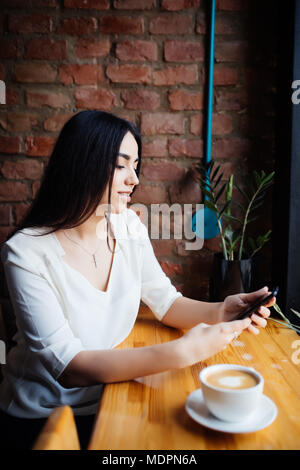 Ritratto di giovane imprenditrice utilizzare il telefono cellulare mentre in seduta confortevole caffetteria durante la pausa di lavoro Foto Stock
