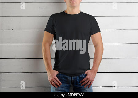 Giovane uomo in una T-shirt nera e jeans blu su bianco sullo sfondo di legno. Parte anteriore mockup vestiti. Foto Stock