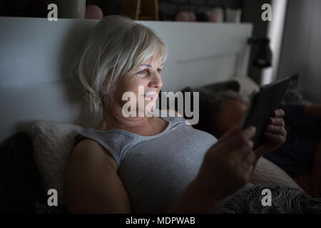 Ritratto di felice senior lady utilizzando tablet a letto Foto Stock