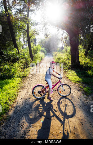 Ragazza su una bicicletta in estate parcheggiare all'esterno, il tramonto. Foto Stock