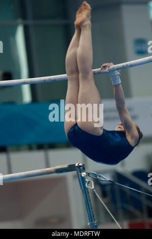 Giovane donna ginnasta appesa su barre irregolari al campionato Foto Stock