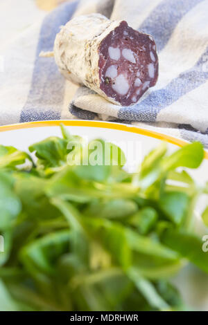 Pezzo di salame salsiccia affumicata in prossimità di una fresca insalata di lattuga Foto Stock