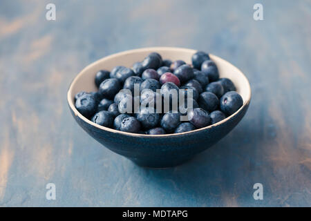 Piccolo recipiente pieno di mirtilli freschi messi sul tavolo dipinte di blu Foto Stock