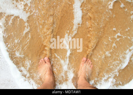 Vista dall'alto di un uomo è la gamba in piedi sulla sabbia e lambita da o Foto Stock