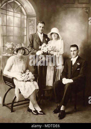 Festa di nozze del Queensland del Nord, 1920-1930. Studio fotografico di una sposa e lo sposo con la loro damigella e miglior uomo. La sposa e lo sposo sono poste dietro un legno intagliato stand, sposa il bouquet in appoggio sul supporto. La damigella e miglior uomo sono seduti nella parte anteriore e su entrambi i lati della coppia di sposi. La sposa e la damigella usura tipico stile anni Venti abiti e cappelli Foto Stock